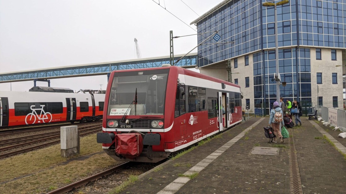 Roter Regionalzug der HANS am Bahnhof in Mecklenburg-Vorpommern; Reisende mit Gepäck warten am Bahnsteig.
